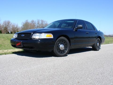 2003 Ford Crown Victoria - Black 2003 Ford Crown Victoria with a 'DARE' plate is parked on a road under a clear blue sky.