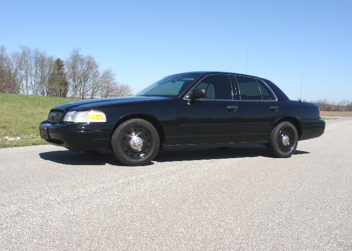 Black Ford Crown Victoria sedan in side profile with black steel wheels on a road.