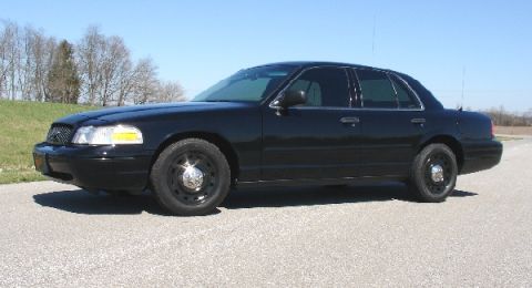 2003 Ford Crown Victoria - A black 2003 Ford Crown Victoria sedan is parked on a paved surface under a clear blue sky.