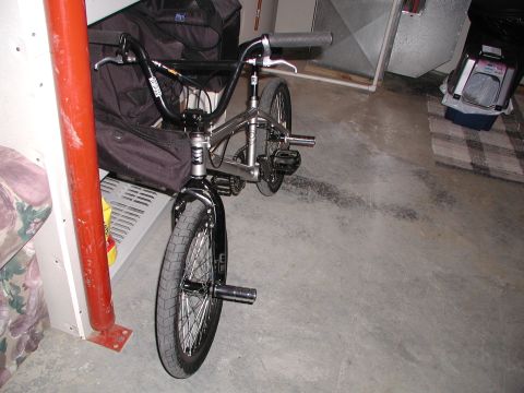 1998 Jeep TJ - BMX bicycle with pegs on front wheel, parked indoors next to bags and a red pole.