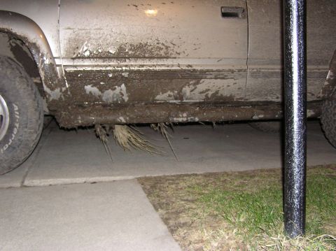 2000 Chevrolet Tahoe - Truck side heavily coated in mud, with debris hanging from the rocker panel and undercarriage.