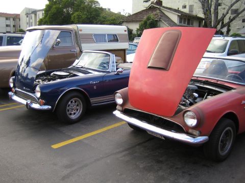 1968 Ford Mustang - Two vintage convertible sports cars are parked side-by-side with their hoods open, revealing their engines.