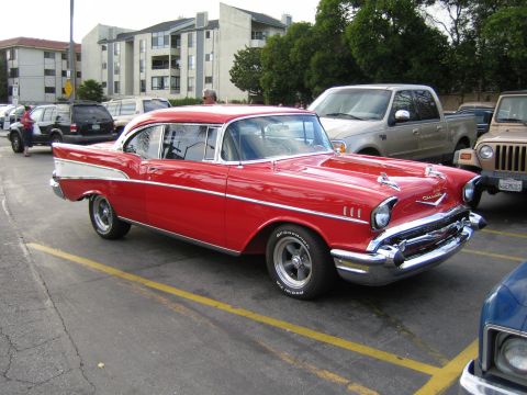 1968 Ford Mustang - A classic red 1957 Chevrolet Bel Air coupe is parked in a lot with other vehicles.