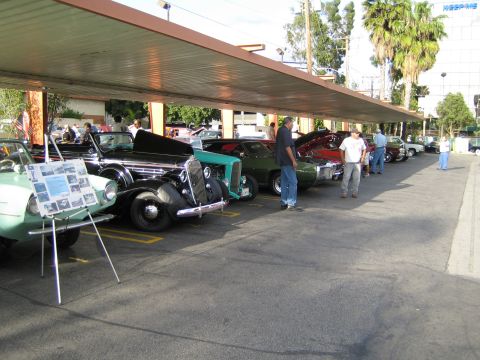 1968 Ford Mustang - Multiple classic cars are parked in a row under a covered area, with a display board in the foreground.