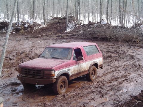 2000 Chevrolet Tahoe - This off-road vehicle is navigating a challenging muddy terrain with dense woods surrounding it.