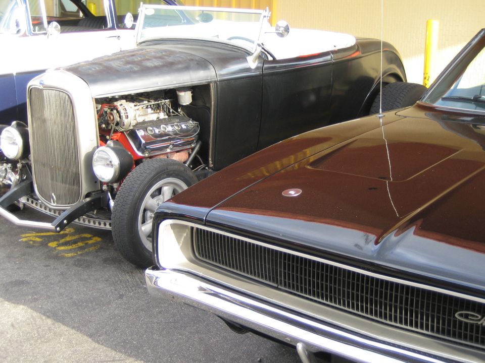 Front view of a dark muscle car next to a hot rod with exposed engine