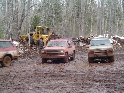 2000 Chevrolet Tahoe - Several vehicles navigate a muddy terrain with trees and debris scattered around.