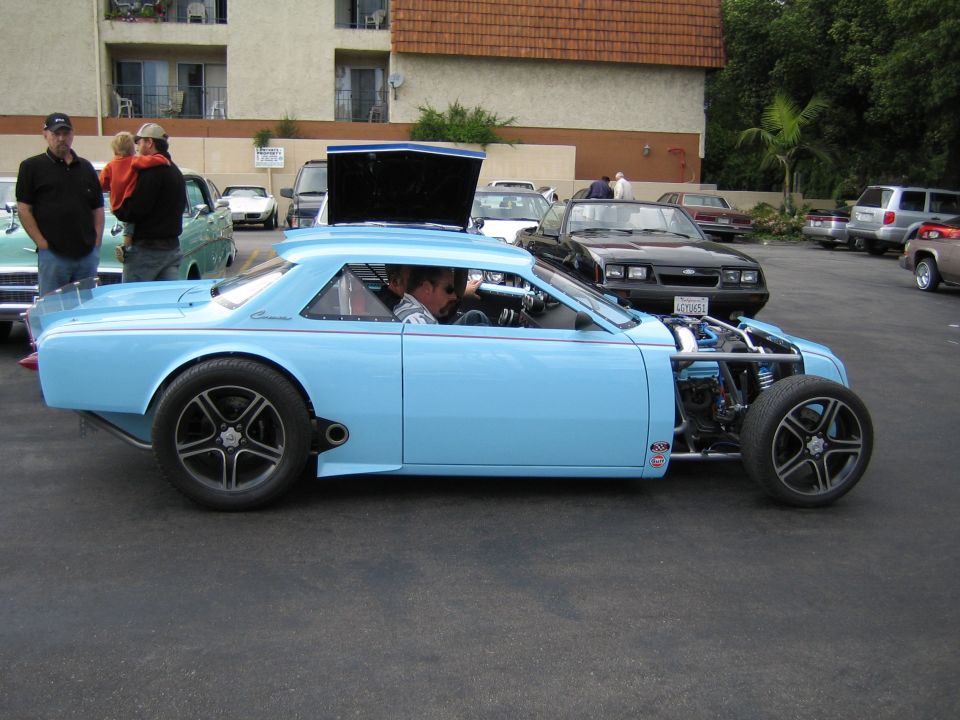 Customized light blue coupe with exposed engine and racing wheels, seen from the side