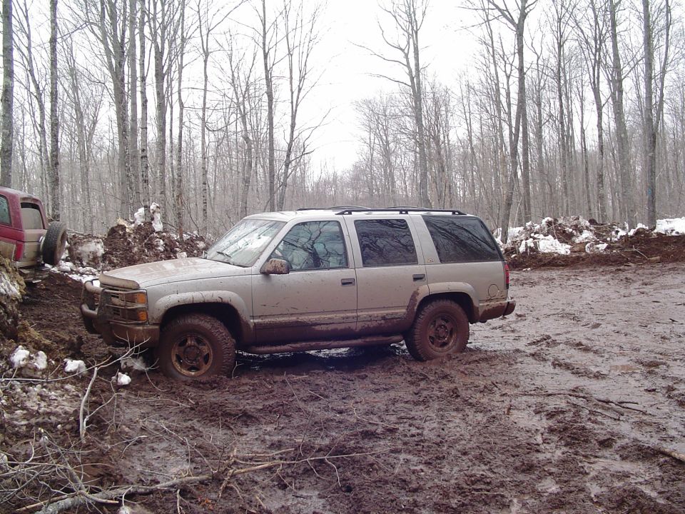 Silver SUV stuck in mud, 3/4 front view. Another vehicle visible to the left