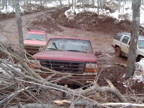 2000 Chevrolet Tahoe - Several vehicles are stuck in a muddy, wooded area with snow on the ground.