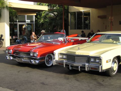 1968 Ford Mustang - Two vintage cars, a red convertible and a yellow coupe, are parked side-by-side under an overhang.