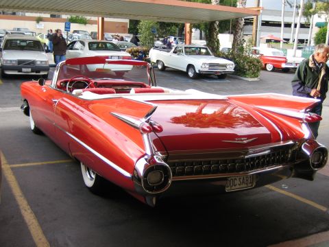 1968 Ford Mustang - A classic red convertible with prominent tail fins is parked in a lot.