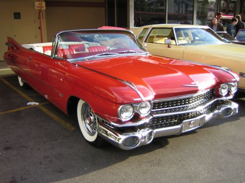 1968 Ford Mustang - A bright red 1959 Cadillac convertible is parked next to a cream-colored sedan.