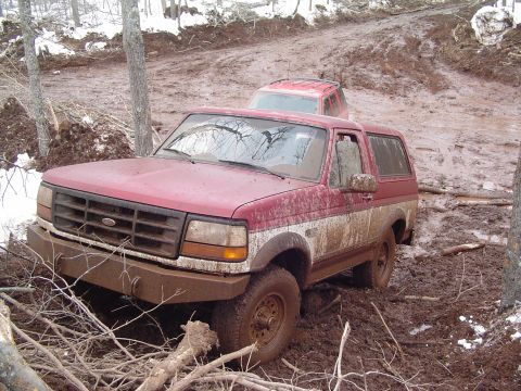 2000 Chevrolet Tahoe - Two off-road vehicles are stuck in deep mud on a wooded trail, with branches and debris scattered around.