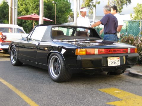 1968 Ford Mustang - A black Porsche 914 is parked on a street, with people standing nearby.