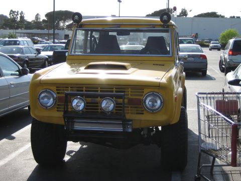 1990 Ford Bronco - Front view of a yellow early Ford Bronco fitted with a grille guard, four round driving lights and roof lights, beside a shopping cart in a…