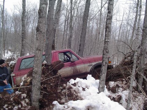 2000 Chevrolet Tahoe - A red pickup truck is stuck in a challenging off-road situation with snow and mud.