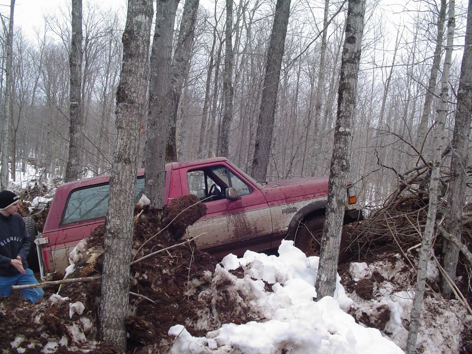 Red pickup truck stuck in a wooded area with snow and mud, side view
