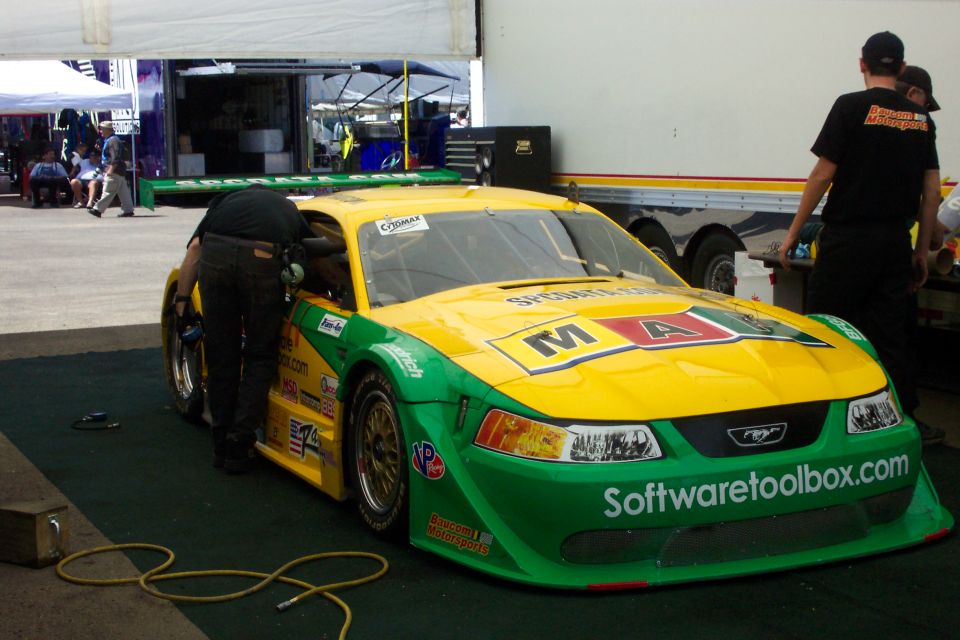 Yellow and green Mustang race car in paddock tent, crew working on it, Softwaretoolbox.com livery