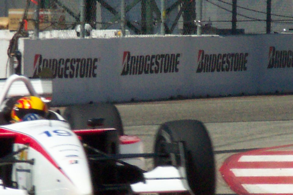 Close shot of white number 19 open-wheel car's front and tire against a Bridgestone barrier wall