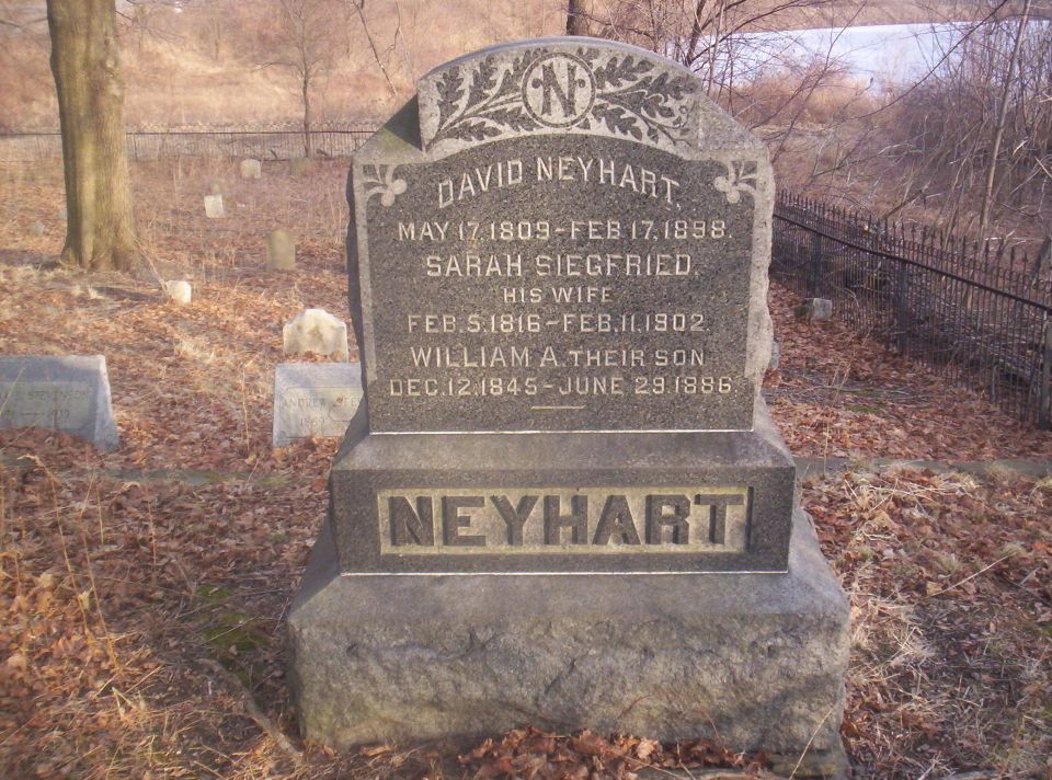 Gravestone with names and dates, surrounded by fallen leaves and other headstones