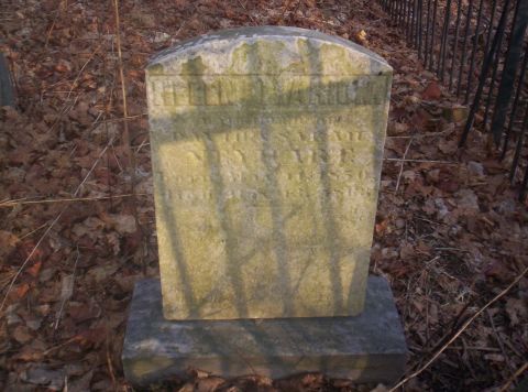 1995 Ford Bronco - A weathered gravestone stands in a cemetery, surrounded by fallen leaves and a metal fence.