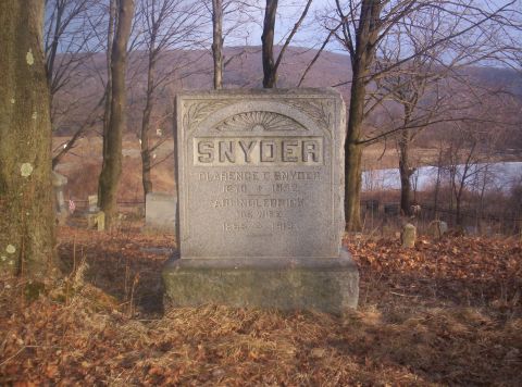 1995 Ford Bronco - A weathered gravestone stands in a cemetery, surrounded by trees and dry leaves, with a body of water visible in the distance.
