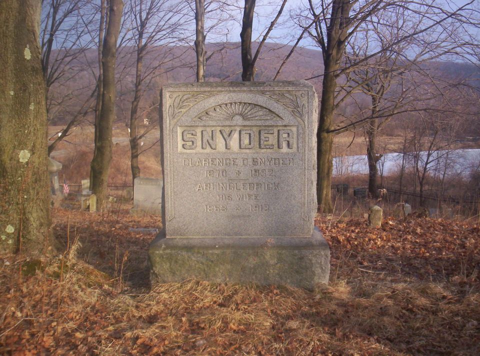 Gravestone for Snyder family in a cemetery with trees and a lake in the background