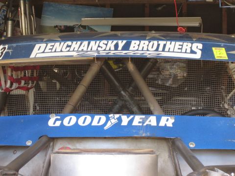 1990 Ford Bronco - Rear deck of a blue off-road race vehicle lettered Penchansky Brothers Racing and Goodyear, with exposed tube chassis bracing inside a gara…