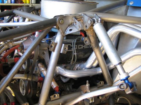 1990 Ford Bronco - Detail of a welded tube chassis surrounding an engine marked Chevy, with braided lines, headers and a blue heim-jointed suspension link.