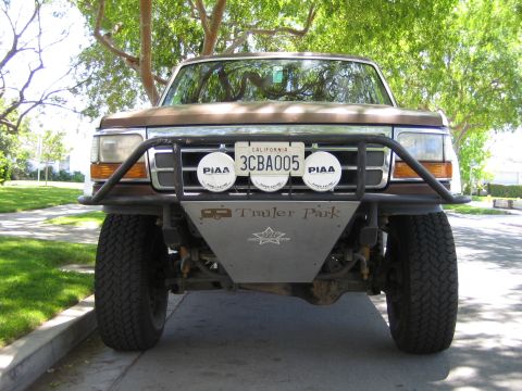 1990 Ford Bronco - Front of a lifted full-size Ford with a prerunner tube bumper, twin PIAA lights, skid plate and California plate 3CBA005, parked on a stree…