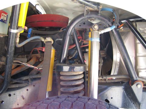 1990 Ford Bronco - Close-up of a front suspension showing a yellow shock, coil spring, red brake rotor, and tube-frame components above a mud tire.