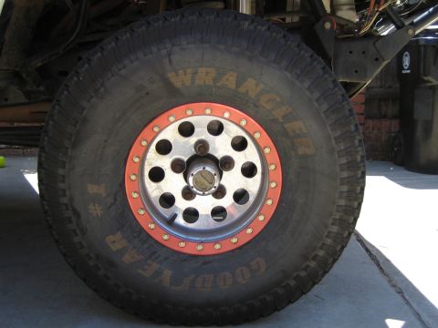 1990 Ford Bronco - Goodyear Wrangler off-road tire mounted on a polished beadlock wheel with a red lock ring.