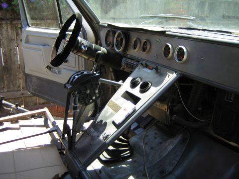 1990 Ford Bronco - Bare interior of a vehicle under construction showing a steering wheel, round gauge cluster, and exposed shifter linkage.