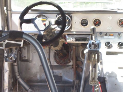 1990 Ford Bronco - Interior of a race-prepped vehicle with a suede steering wheel, multiple gauges, roll-cage tubing, and twin shifters.