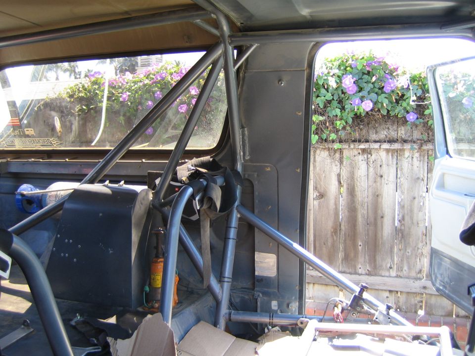 Roll-cage tubing inside a stripped vehicle with view to flowering fence outside