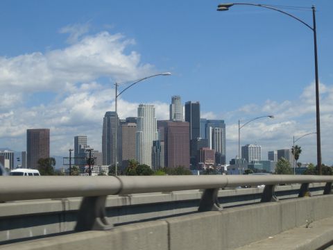 1990 Ford Bronco - city skyline of high-rise towers under blue sky with clouds, viewed from a freeway behind a guardrail and streetlights.