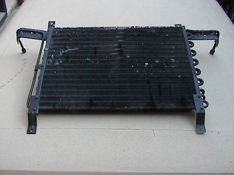 1989 Ford Bronco - A black radiator or condenser unit, likely for a vehicle, is shown with its mounting brackets and coiled tubing.