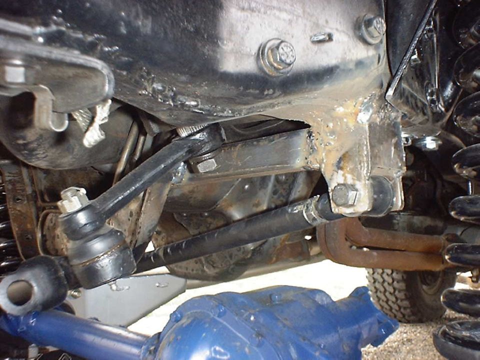 Close-up of vehicle suspension linkage and steering components, with a partial view of a tire and blue differential