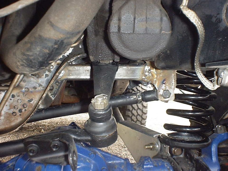Close-up of a vehicle's steering linkage and suspension, showing a ball joint, tie rod, and coil spring