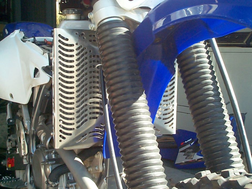 Motorcycle radiator guard and ribbed front fork boots on a blue and white dirt bike