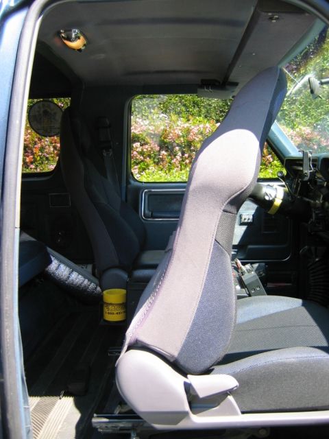 1985 Ford Bronco - The interior of a blue truck shows aftermarket seats and a yellow container on the floor.