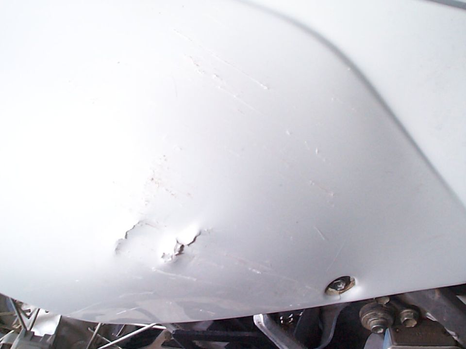 White motorcycle fender with a dent and scratches, showing a screw hole