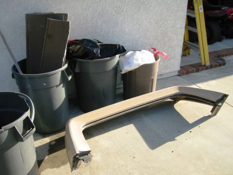 1985 Ford Bronco - A tan car part rests on the ground near several trash cans filled with debris.