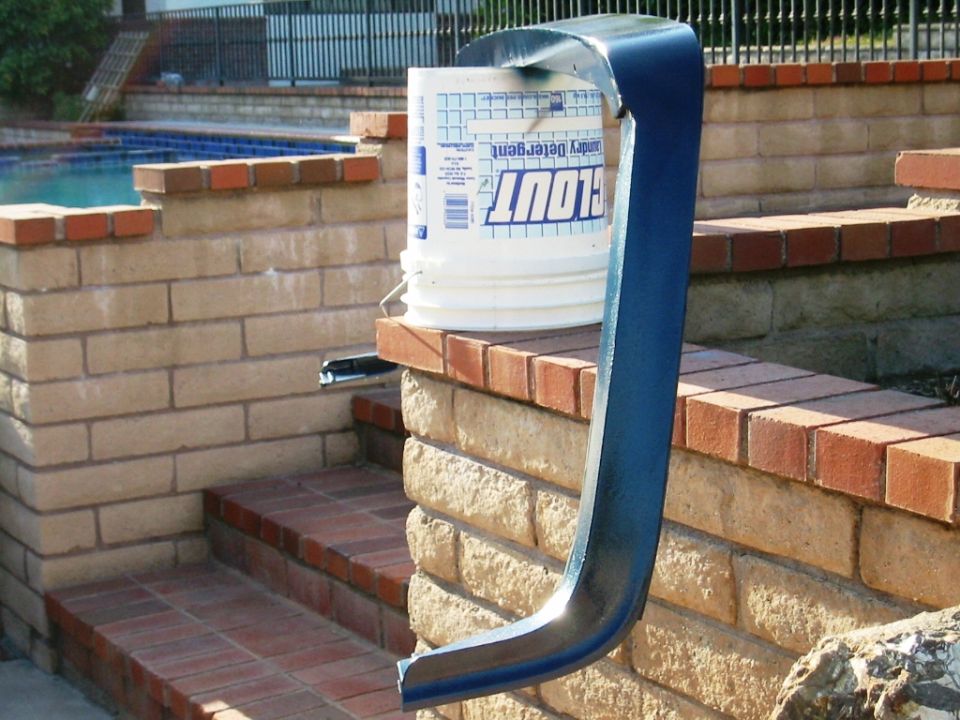 Curved dark metal part on brick wall beside a white detergent bucket