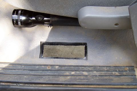 1994 Ford F-150 - A Maglite flashlight is placed on the floor of a vehicle, next to a rectangular opening in the floor panel.