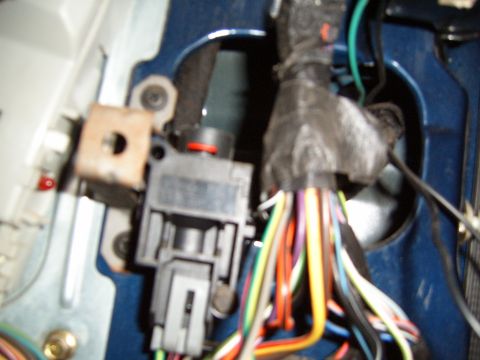 1993 Ford Bronco - Extreme close-up of the door-jamb wiring pass-through on a blue truck body, with a bundle of colored wires fanning out of a black rubber gr…