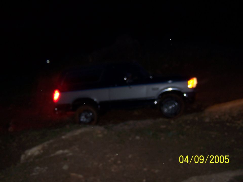 Ford Bronco parked on dirt at night, headlights and taillights on
