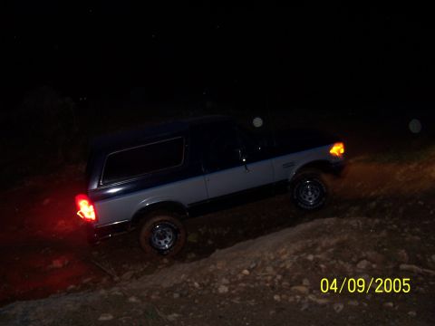 1979 Ford F-150 - A two-tone Ford Bronco navigates a dirt path in the dark, with its brake lights illuminated.