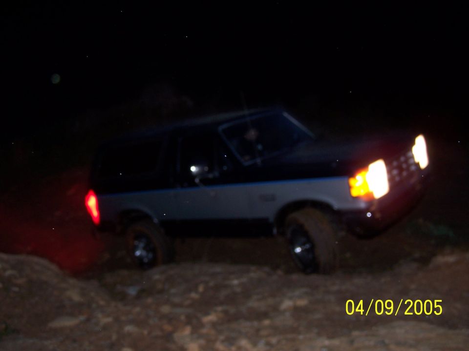Two-tone black and grey Ford Bronco with a blue stripe, driving off-road at night